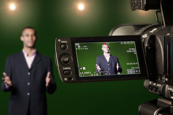 Man in blazer jacket standing in front of a video camera