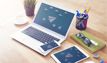 Table with computer, tablet, phone, and office supplies.