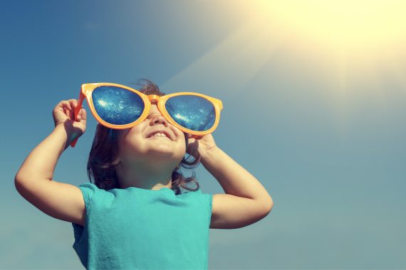 Child looking through oversized plastic glasses toward the sun