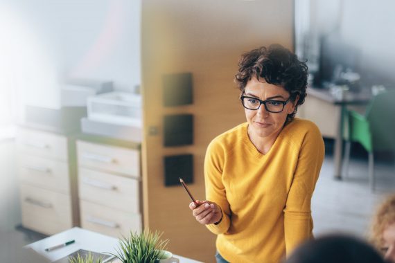 Woman wearing a yellow sweater holding a pencil at a meeting