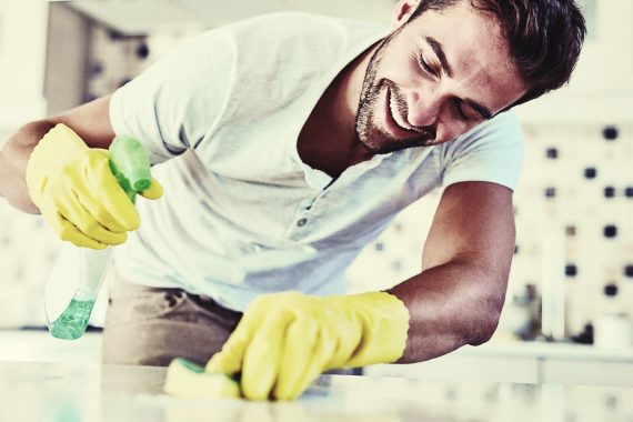 Man cleaning counter with spray bottle and sponge wearing yellow gloves
