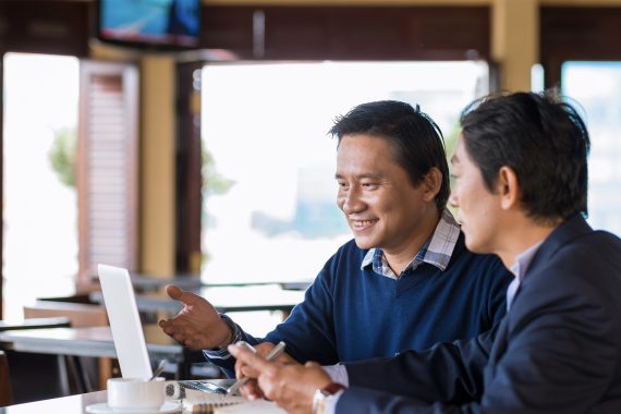 Business meeting with two happy people at a cafe table with computer.
