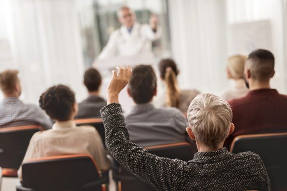 Person raising their hand in the audience of a medical professional presentation.
